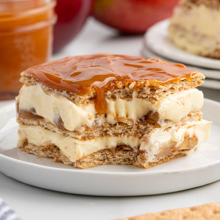 A square slice of Caramel Apple Eclair Cake with creamy vanilla filling and caramel sauce on top, served on a white plate. The layers appear to be crispy wafers and smooth cream.