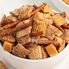 Close-up of homemade churro Chex Mix in a white bowl with pretzels and caramel pieces.