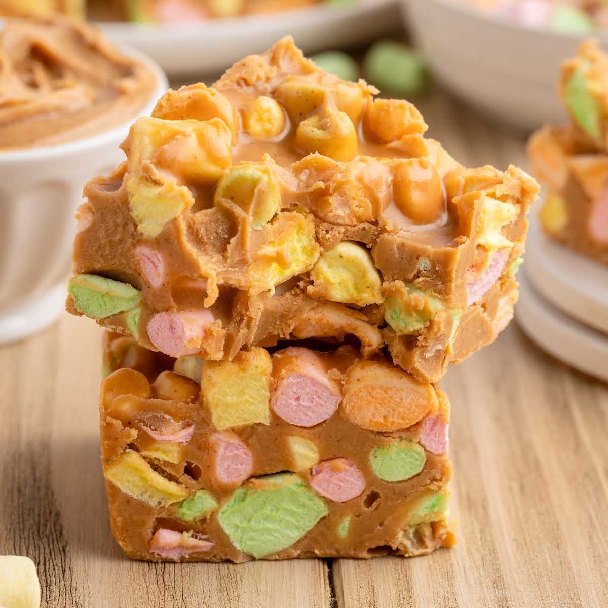 Stack of colorful peanut butter marshmallow squares on a wooden surface showing soft, chewy texture and pastel mini marshmallows.