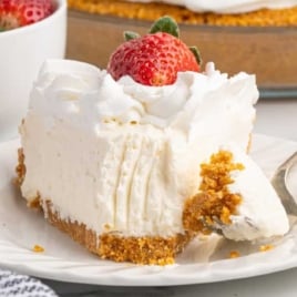No bake cheesecake with graham cracker crust topped with whipped cream and fresh strawberries in a glass pie dish