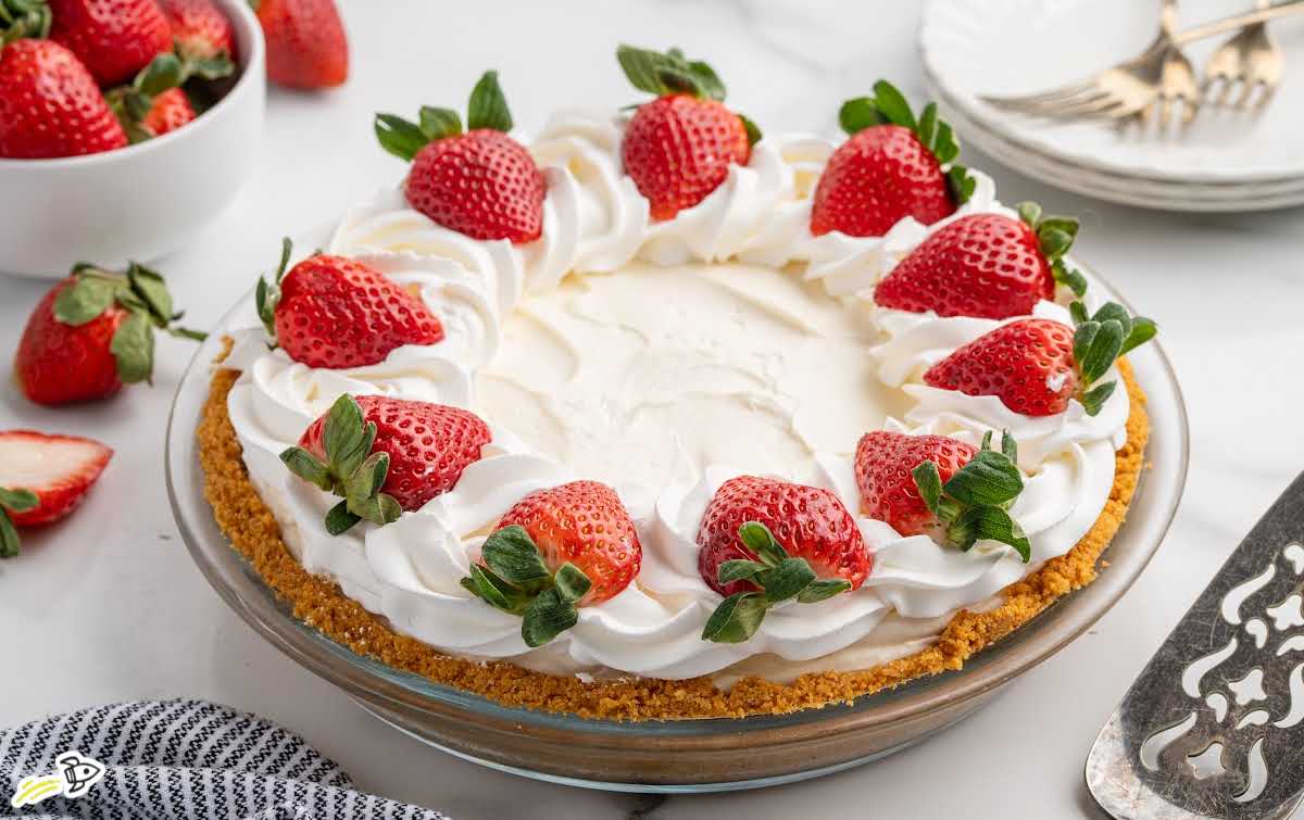 No bake cheesecake slice lifted from the pie pan with whipped cream and strawberry topping