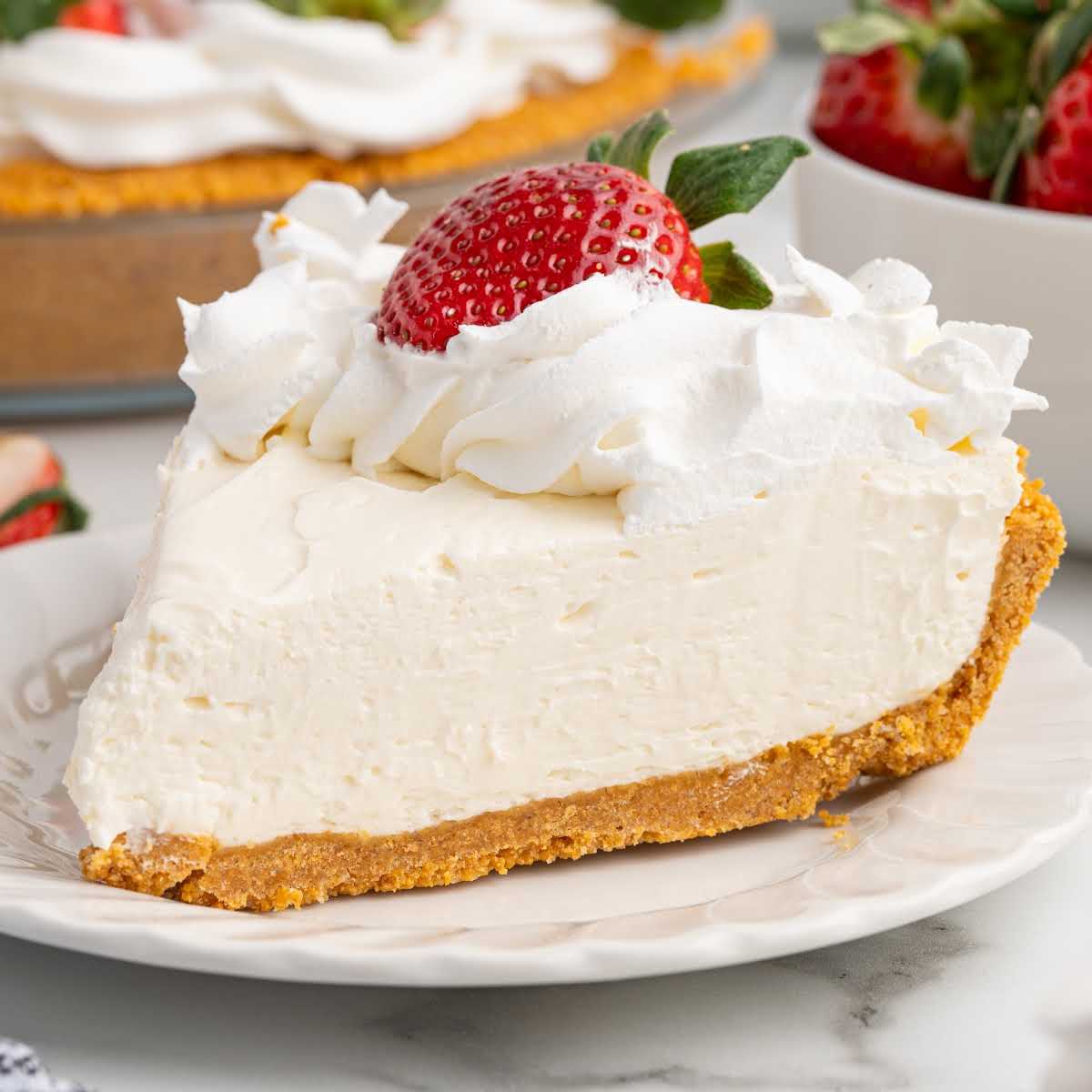 Single slice of no bake cheesecake with whipped topping and fresh strawberry on a white plate
