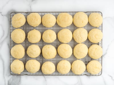 Twenty-four round, golden Sour Cream Cookies are arranged in a grid pattern on a cooling rack, set on a white marble surface.