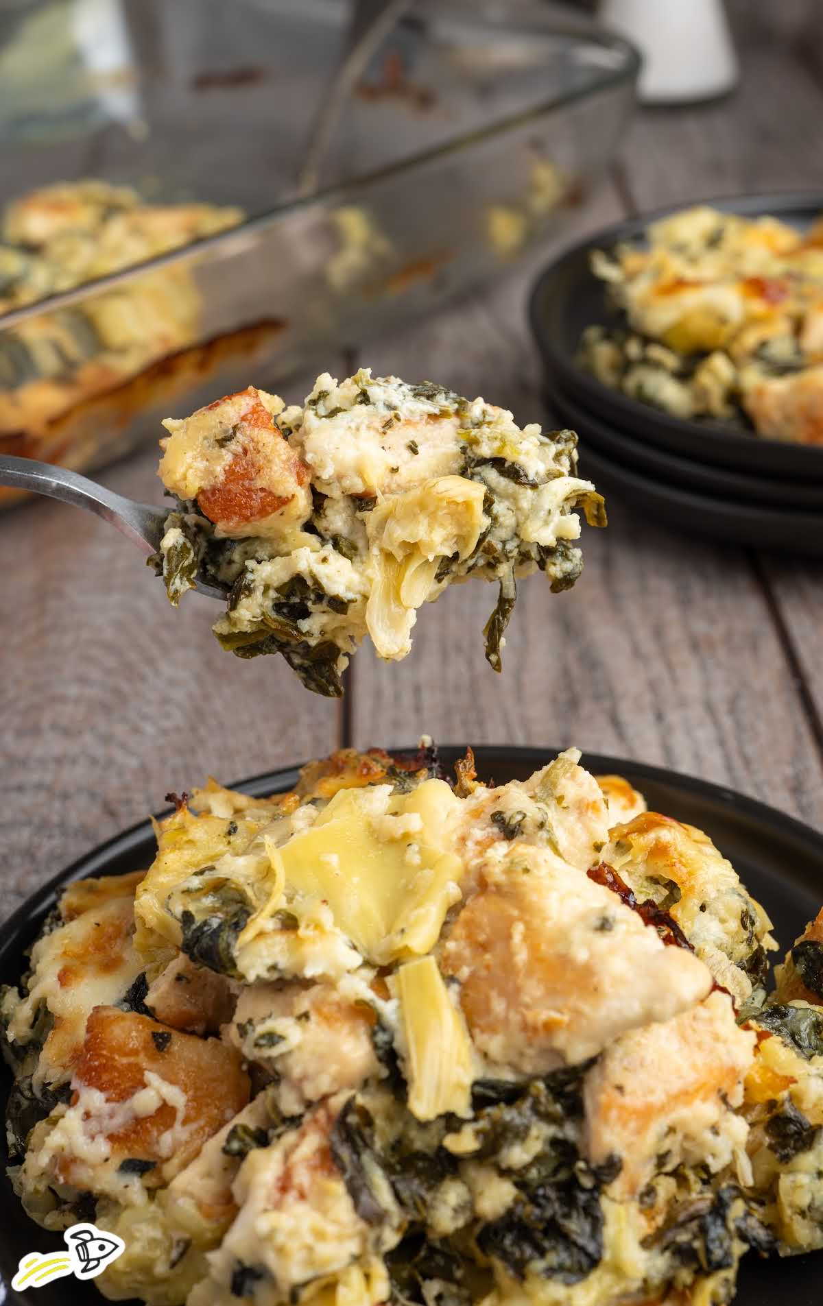 Spoonful of creamy spinach and artichoke chicken casserole with chunks of chicken and artichoke hearts.