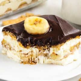 A piece of banana eclair cake on a white plate with a bite out of it.