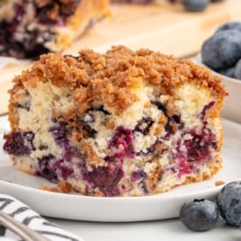 A slice of Blueberry Coffee Cake on a white plate with a fork.