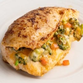 Golden brown stuffed chicken breast filled with broccoli, carrots, and melted cheese on a dinner plate.