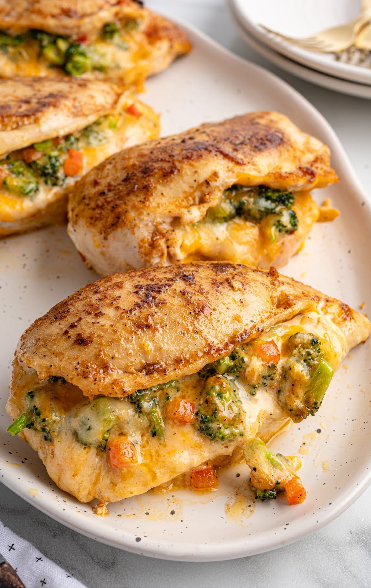 Golden brown stuffed chicken breasts filled with broccoli, carrots, and melted cheese on a dinner plate.