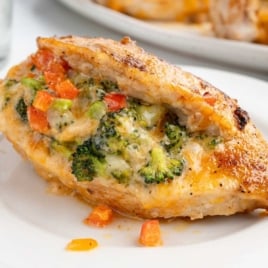 Single serving of cheesy stuffed chicken breast filled with broccoli and diced red bell pepper on a white plate.