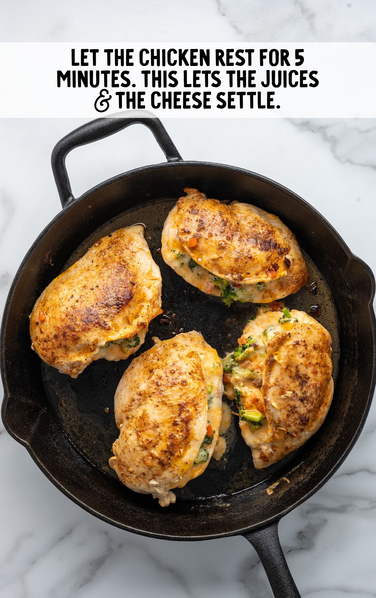 Overhead view of cooked broccoli and cheese stuffed chicken breasts in a cast iron skillet, resting after cooking, with a text overlay instructing to let the chicken rest for 5 minutes.