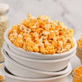 White bowls are stacked, and the top one is full of cheese popcorn.