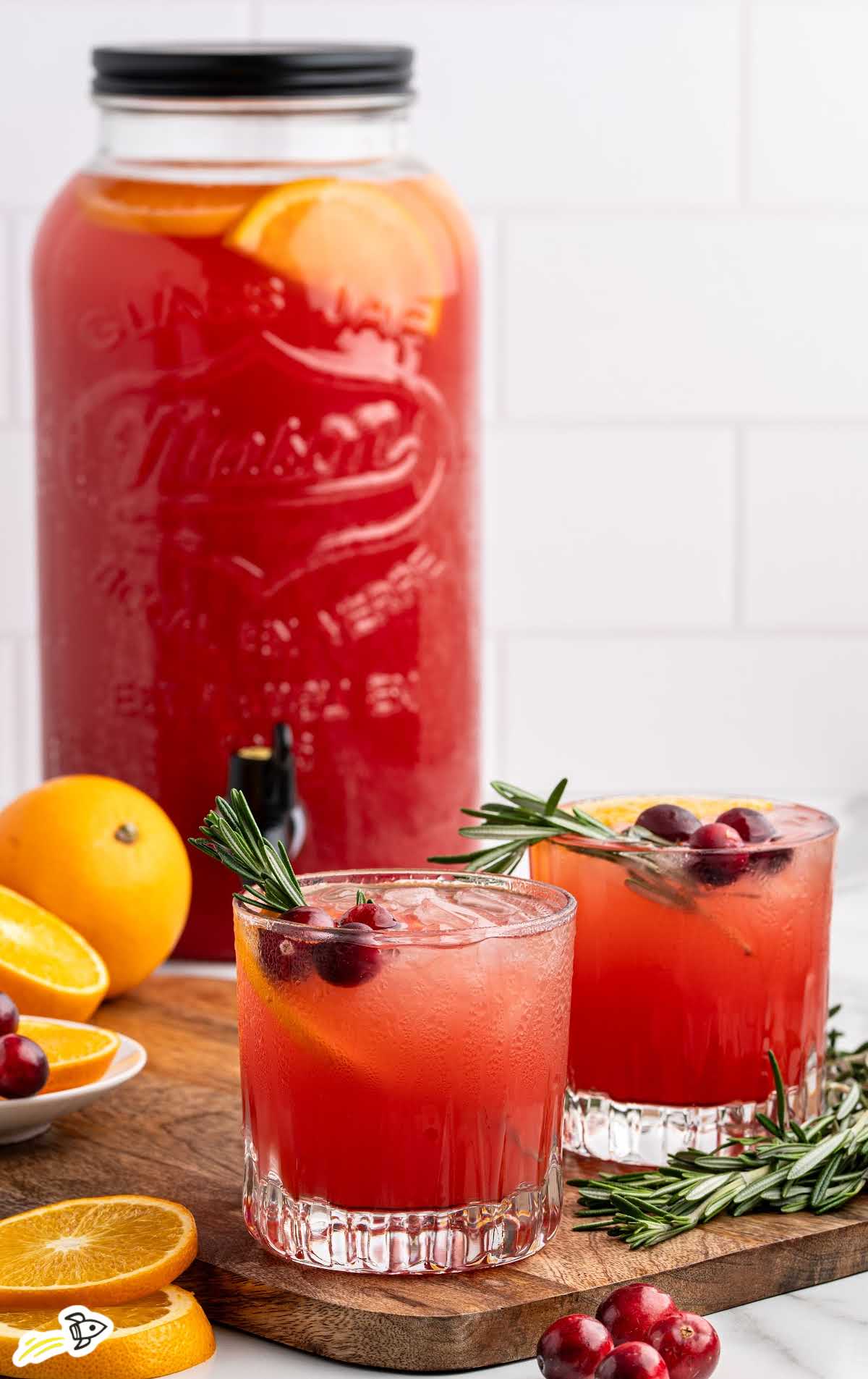 Bright red Christmas morning punch in a large glass drink dispenser with orange slice garnish