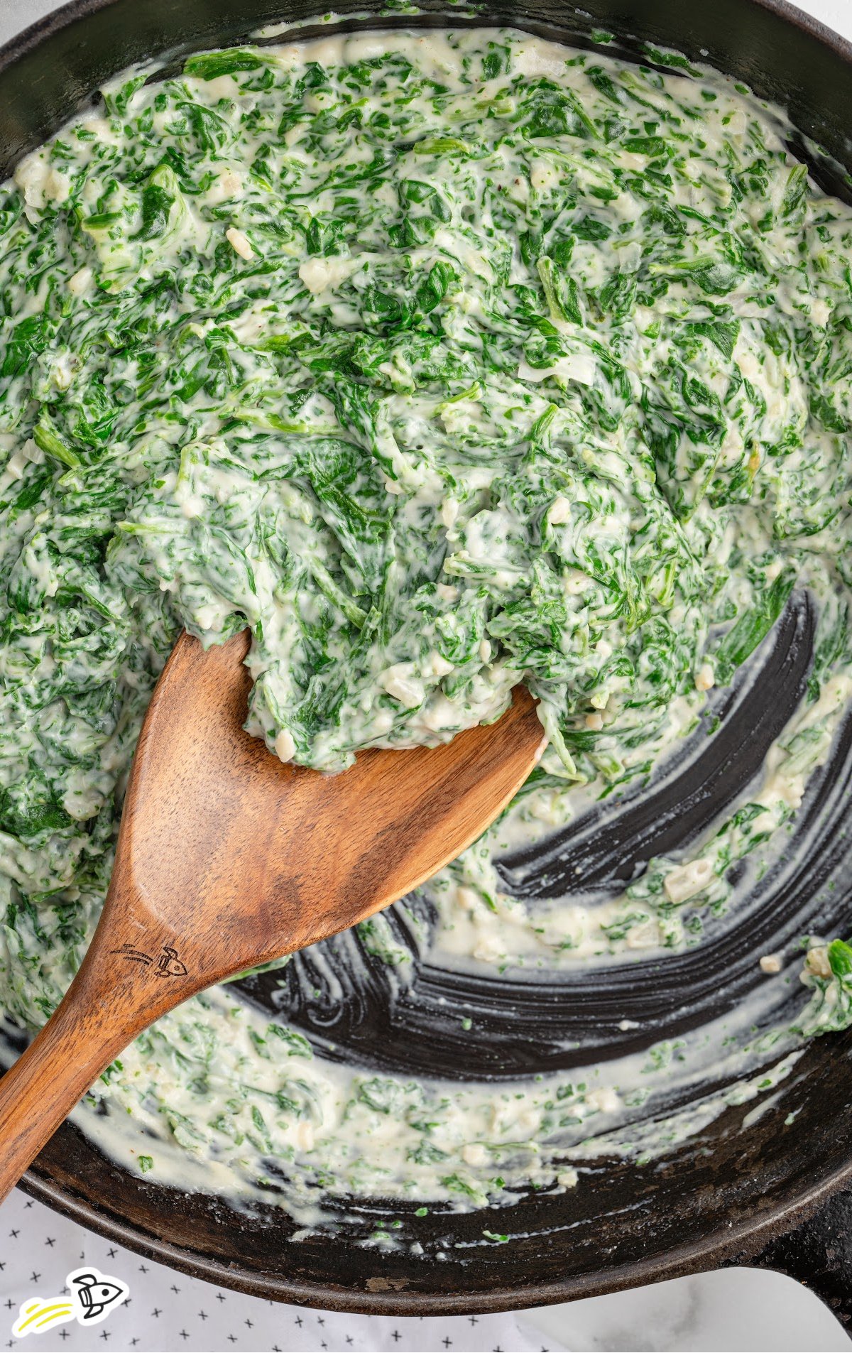 a skillet of creamed spinach with a wooden spoon