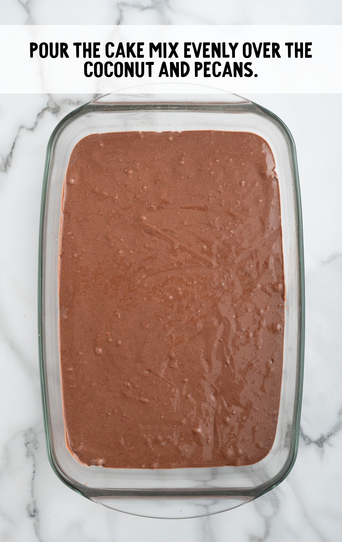 cake batter poured over the coconut and pecans in a baking dish