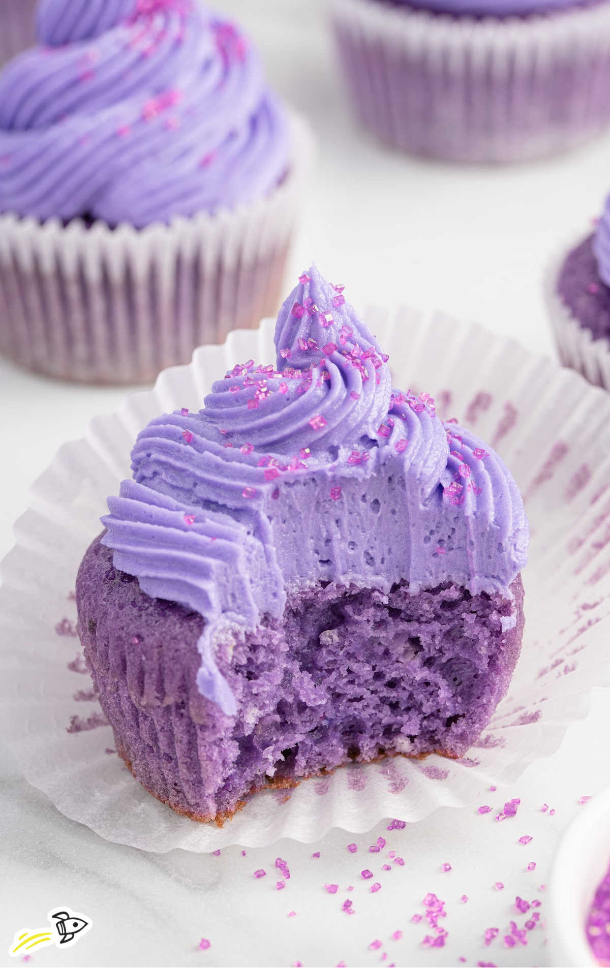 close up shot of frosted Grape Soda Cupcakes with a bite taken out of one of the cupcakes