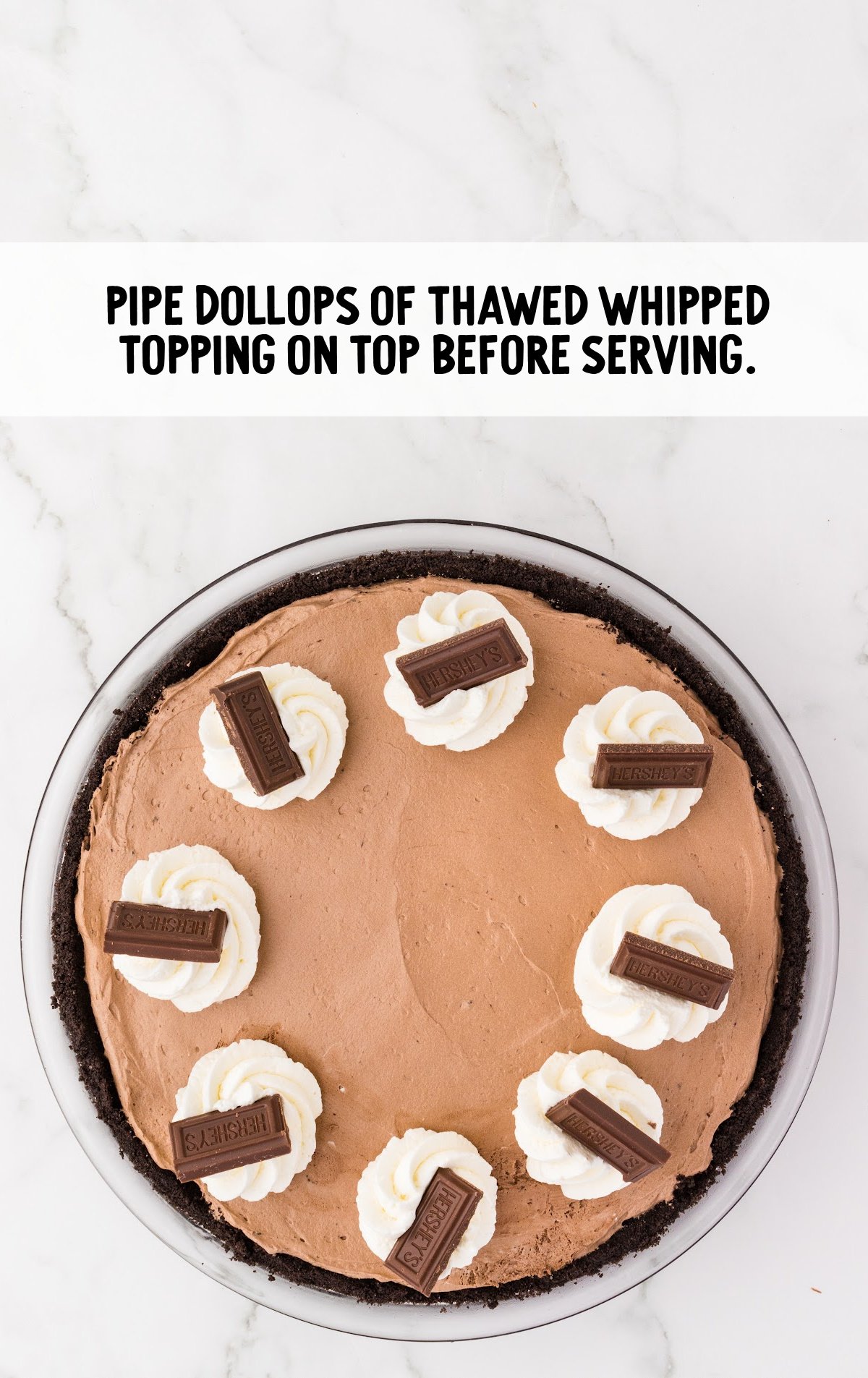 The top of the pie is decorated with whipped cream ad pieces of hershey bar.