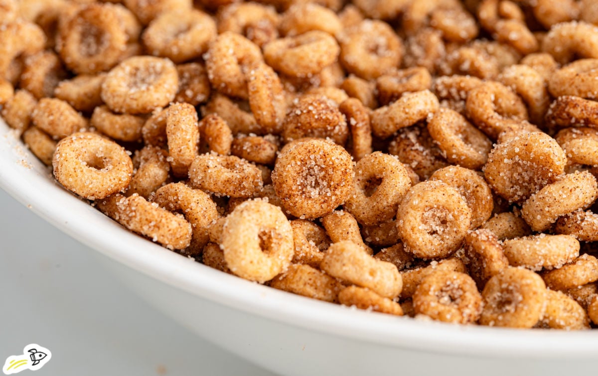 Close-up of hot buttered Cheerios coated in cinnamon sugar, served in a white bowl. The cereal pieces look crisp and golden with a sweet, crunchy coating