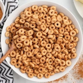 A white bowl full of hot buttered cheerios with a spoon in it.