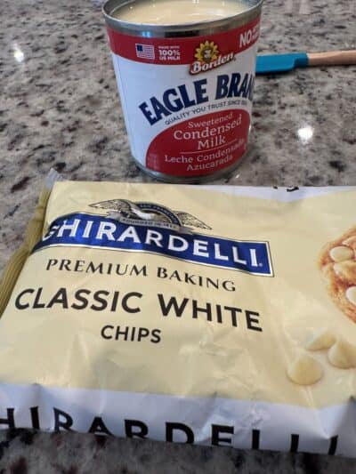 A bag of Ghirardelli Classic White Chips and a can of Eagle Brand sweetened condensed milk on a granite countertop.