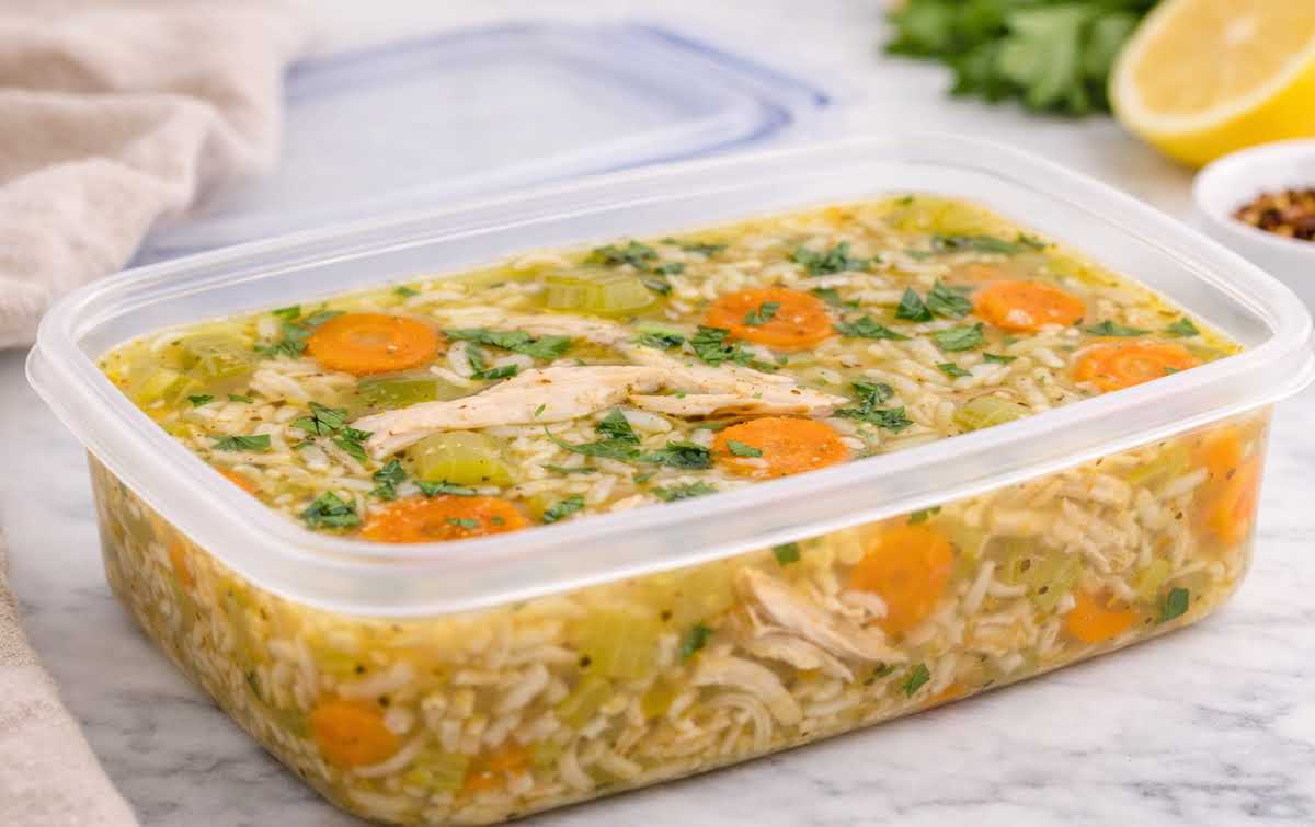 Chicken and rice soup stored in a rectangular airtight container with visible carrots, celery, and shredded chicken
