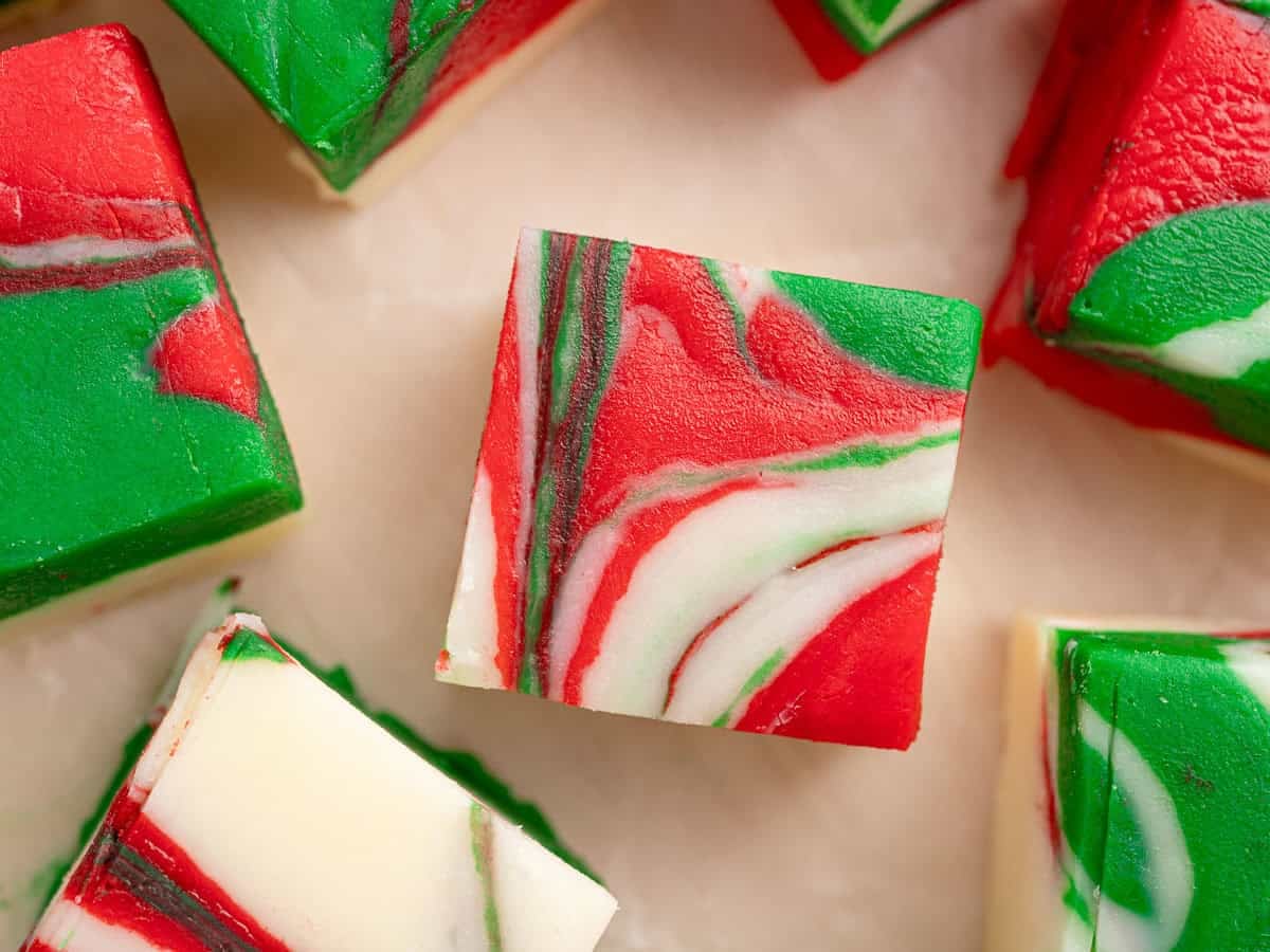 Colorful square holiday fudge pieces with swirled red, green, and white patterns are arranged on a light marble surface. This Christmas Fudge Recipe boasts a creamy texture and vibrant colors, creating a festive appearance perfect for your holiday celebrations.