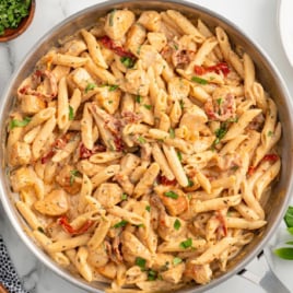 a skillet of chicken pasta garnished with basil