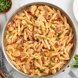 a skillet of chicken pasta garnished with basil