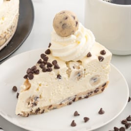 a slice of Cookie Dough Cheesecake topped with chocolate chips, whipped cream, and a cookie dough ball on a plate