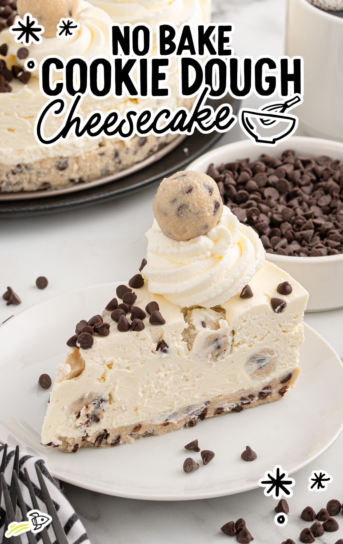 a slice of Cookie Dough Cheesecake topped with chocolate chips, whipped cream, and a cookie dough ball on a plate