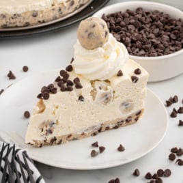 a slice of Cookie Dough Cheesecake topped with chocolate chips, whipped cream, and a cookie dough ball on a plate