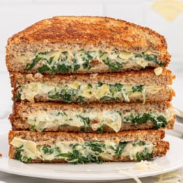 slices of spinach artichoke grilled cheese stacked on top of each other on a plate