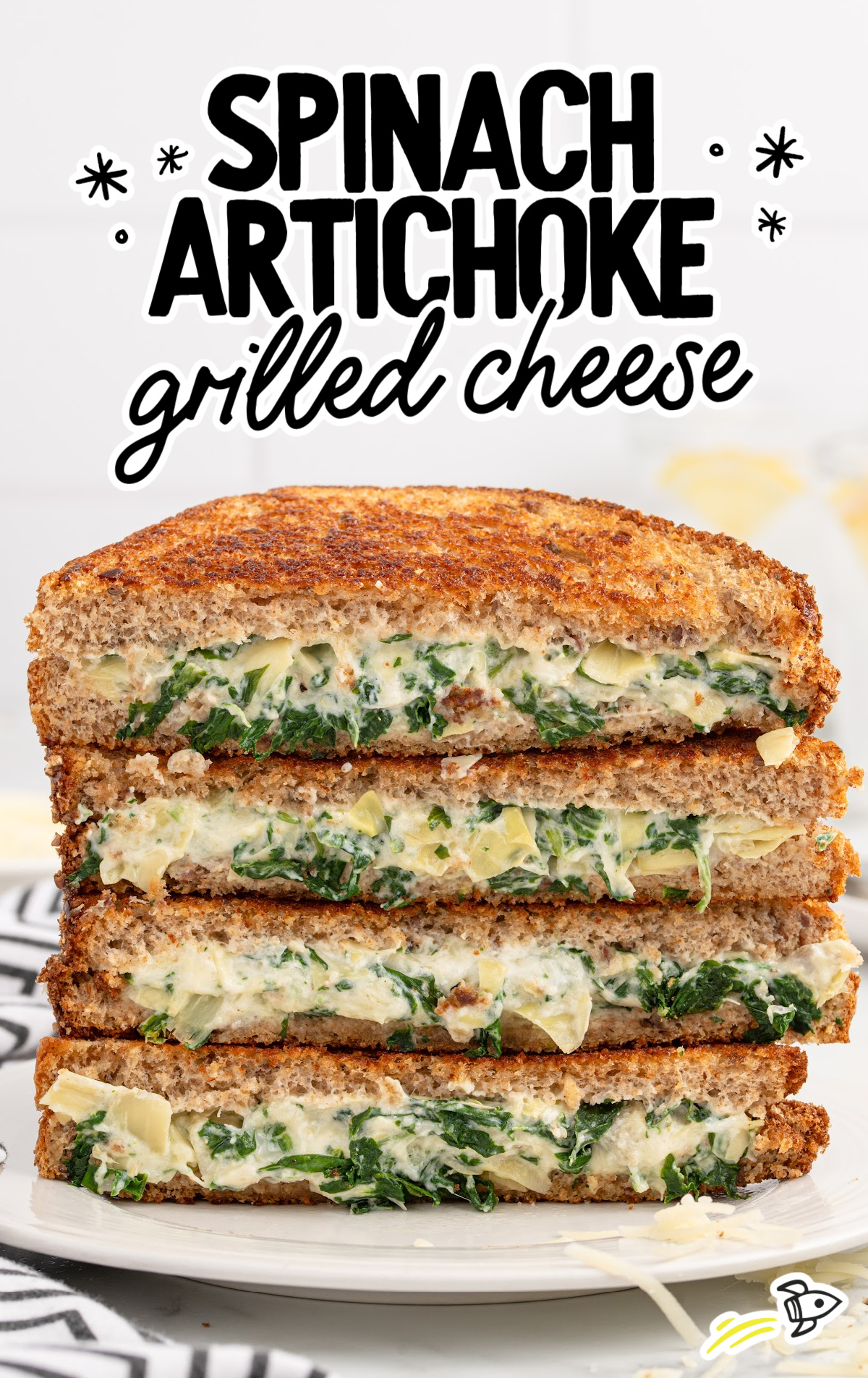 slices of spinach artichoke grilled cheese stacked on top of each other on a plate