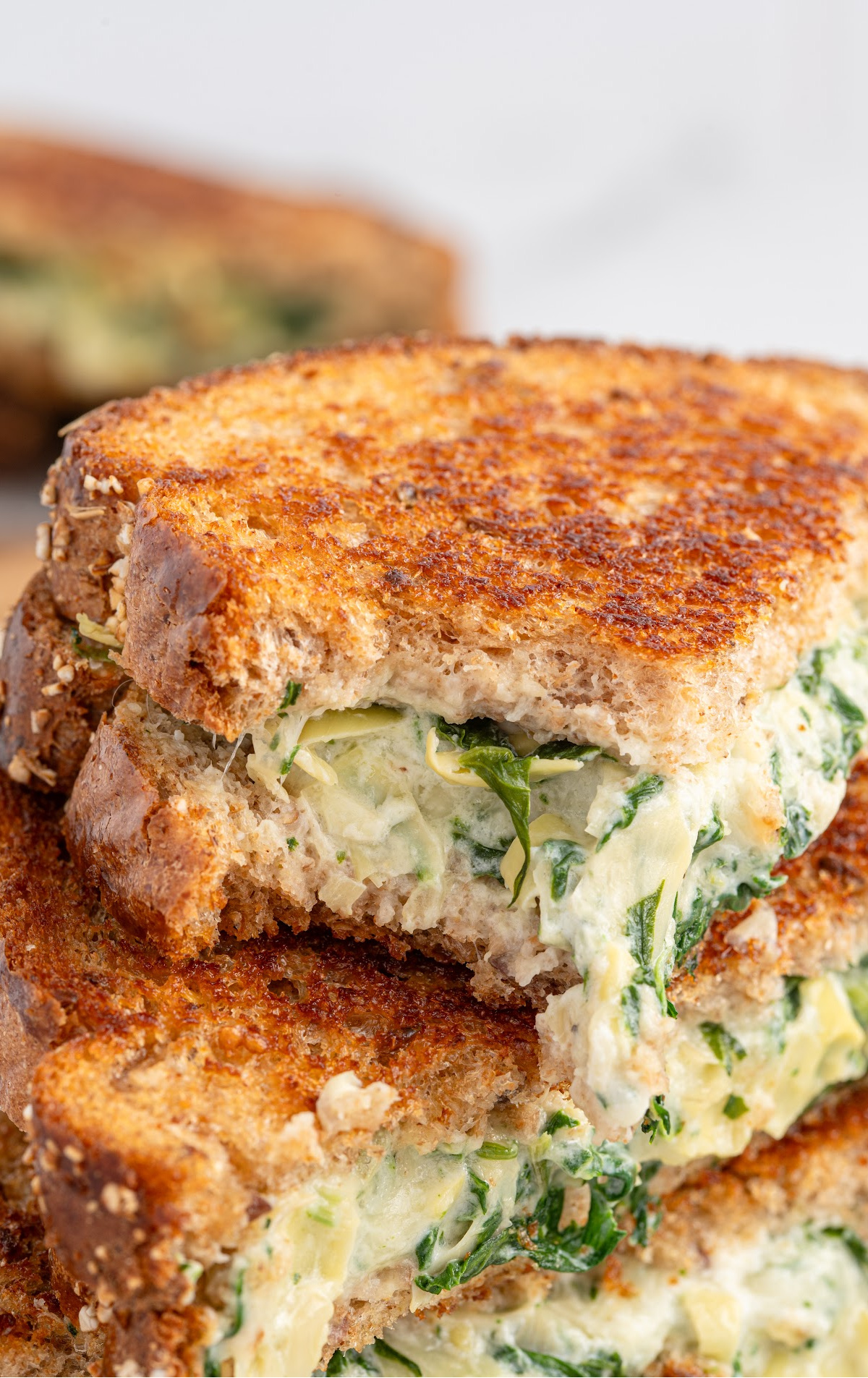 slices of spinach artichoke grilled cheese stacked on top of each other