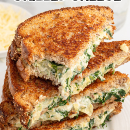 slices of spinach artichoke grilled cheese stacked on top of each other on a plate