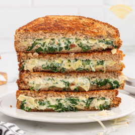 slices of spinach artichoke grilled cheese stacked on top of each other on a plate