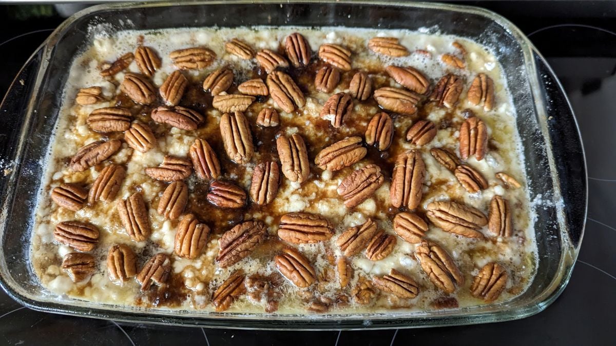 A glass baking dish filled with a creamy Pecan Dump Cake, topped with whole pecans and sprinkled with brown sugar, fresh out of the oven.