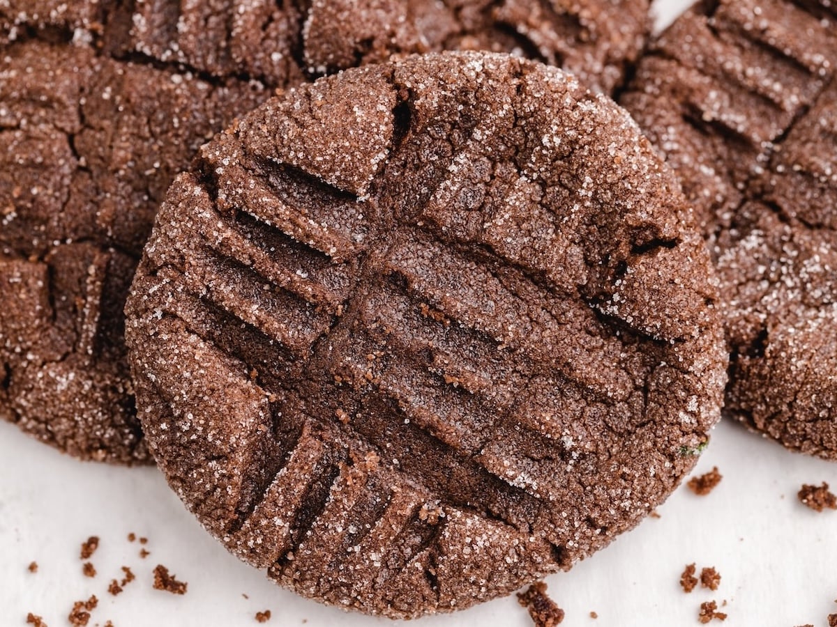 A close-up of Chocolate Peanut Butter Cookies with a crisscross fork pattern on top and a coating of sugar, resting on a white surface—perfect for trying your favorite Chocolate Peanut Butter Cookies Recipe.