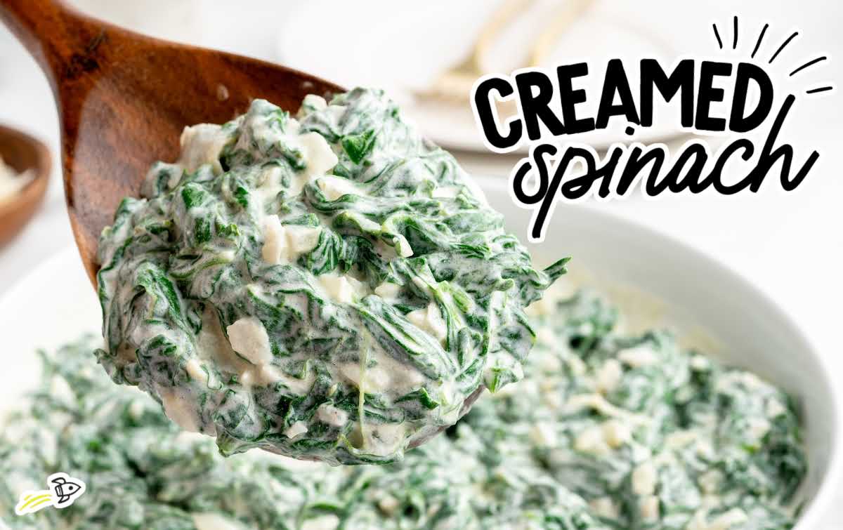 Creamed spinach being scooped with a wooden spoon, showing creamy texture and chopped onions.