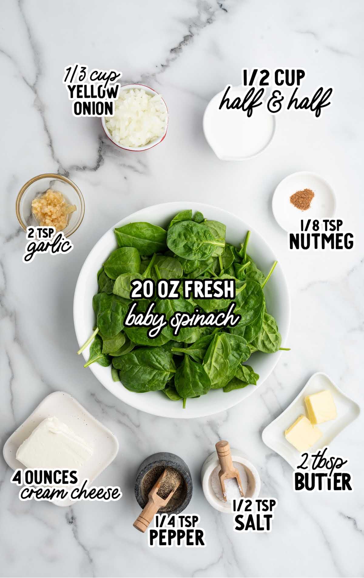 Overhead view of creamed spinach ingredients including fresh baby spinach, cream cheese, onion, garlic, nutmeg, butter, half and half, salt, and pepper.