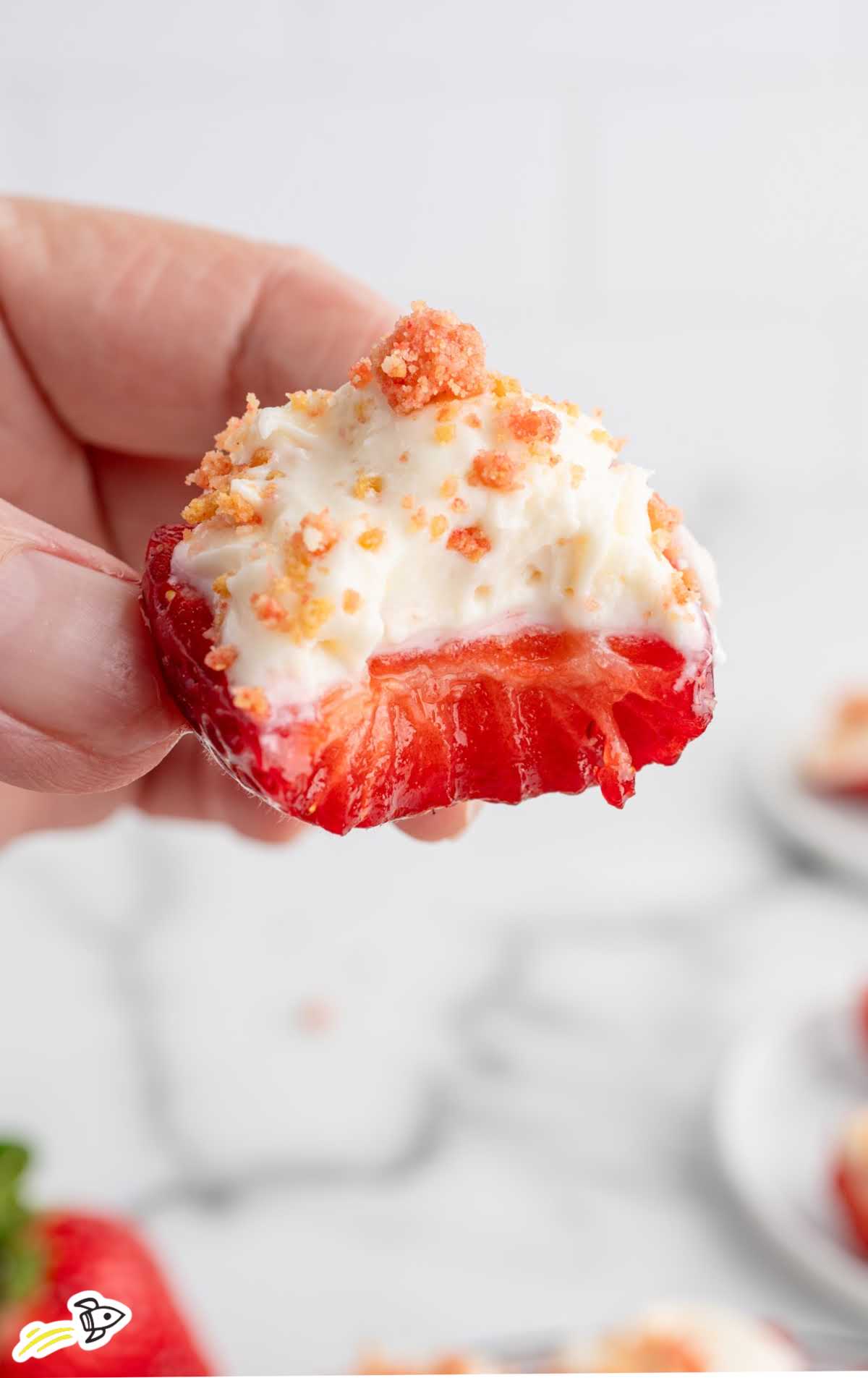 Hand holding a deviled strawberry filled with cheesecake filling and strawberry crunch topping