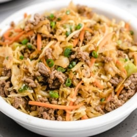 A white bowl filled with a mixture of cooked ground meat, shredded cabbage, carrots, and sliced green onions, this Egg Roll in a Bowl recipe brings your favorite flavors together without the wrapper.