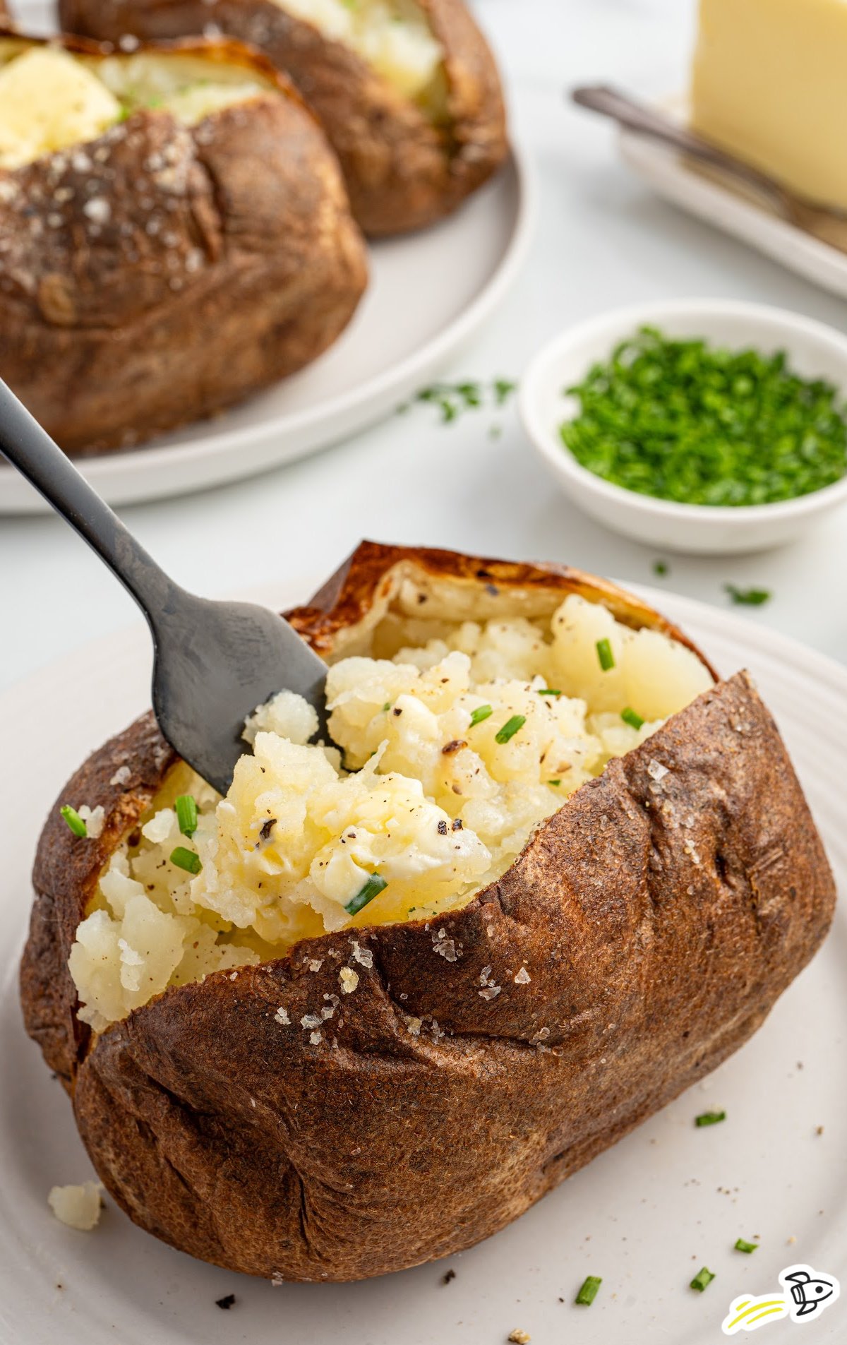 a baked potato topped with chives on a plate with a fork