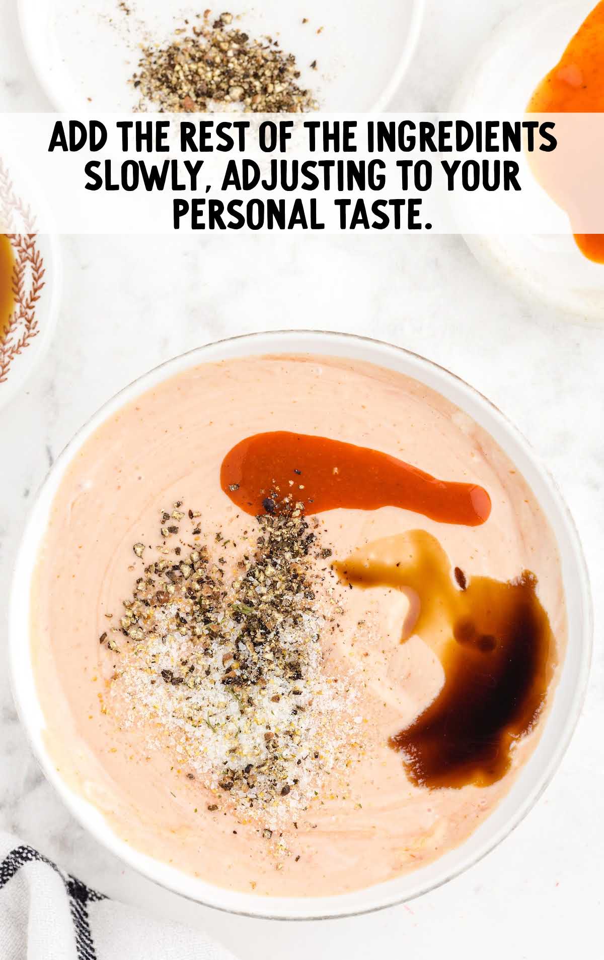 Bowl of sauce topped with hot sauce, Worcestershire, pepper, and garlic salt with text overlay “Add the rest of the ingredients slowly, adjusting to your personal taste.”