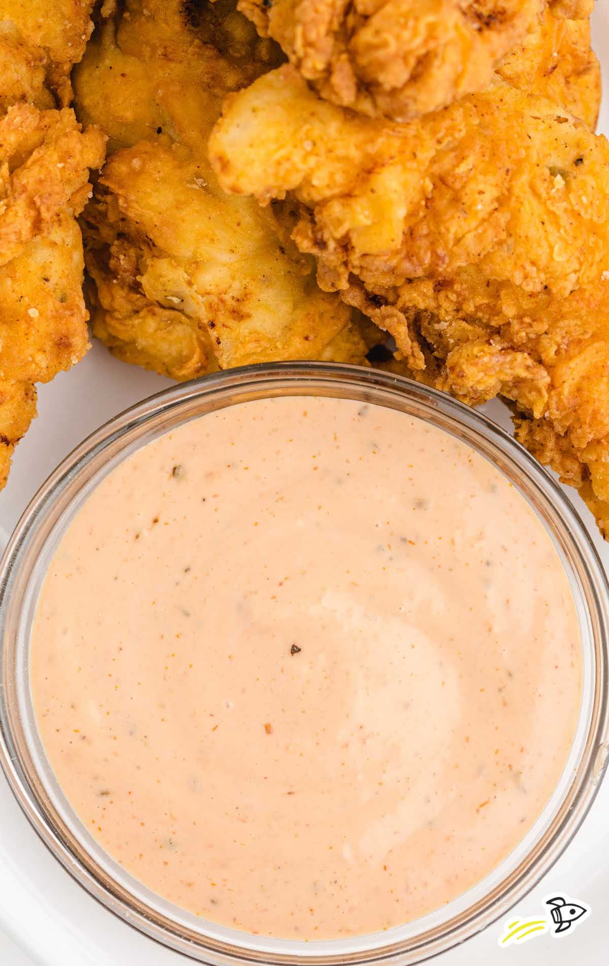 Zoomed-in view of a bowl of creamy dipping sauce surrounded by crispy chicken fingers.