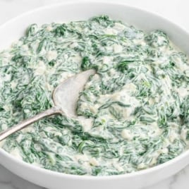 Close-up of creamy spinach mixture on a wooden spoon above a serving bowl.