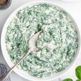 Overhead view of a serving bowl filled with creamy spinach mixture with spoon.