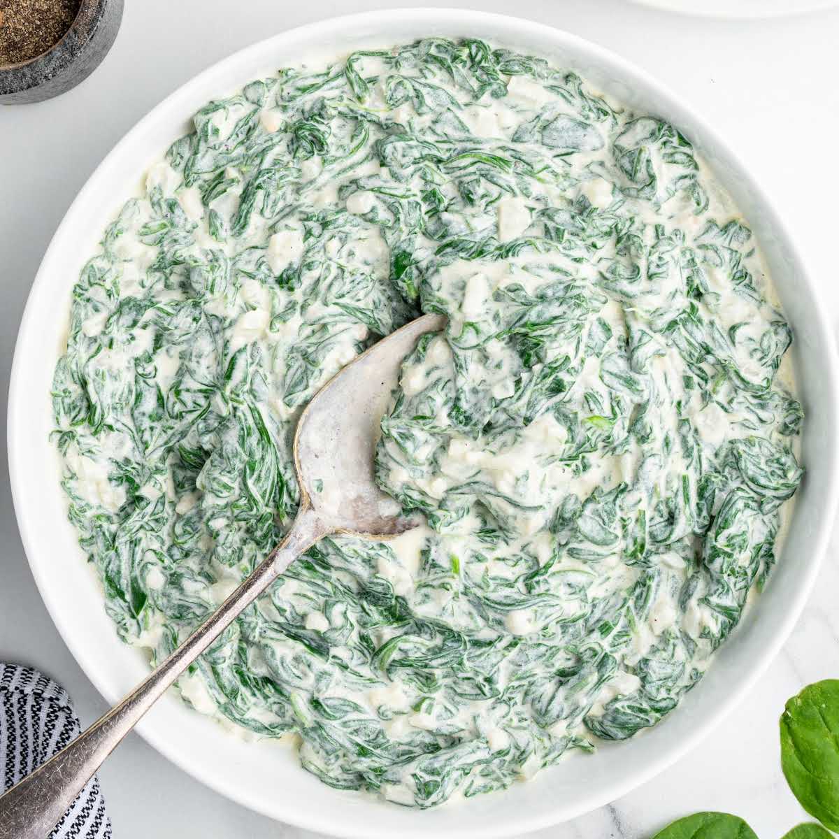 Overhead view of a serving bowl filled with creamy spinach mixture with spoon.