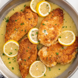 a skillet of Lemon Chicken topped with lemon slices and garnished with parsley