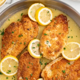 a skillet of Lemon Chicken topped with lemon slices and garnished with parsley