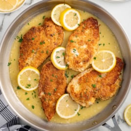 a skillet of Lemon Chicken topped with lemon slices and garnished with parsley